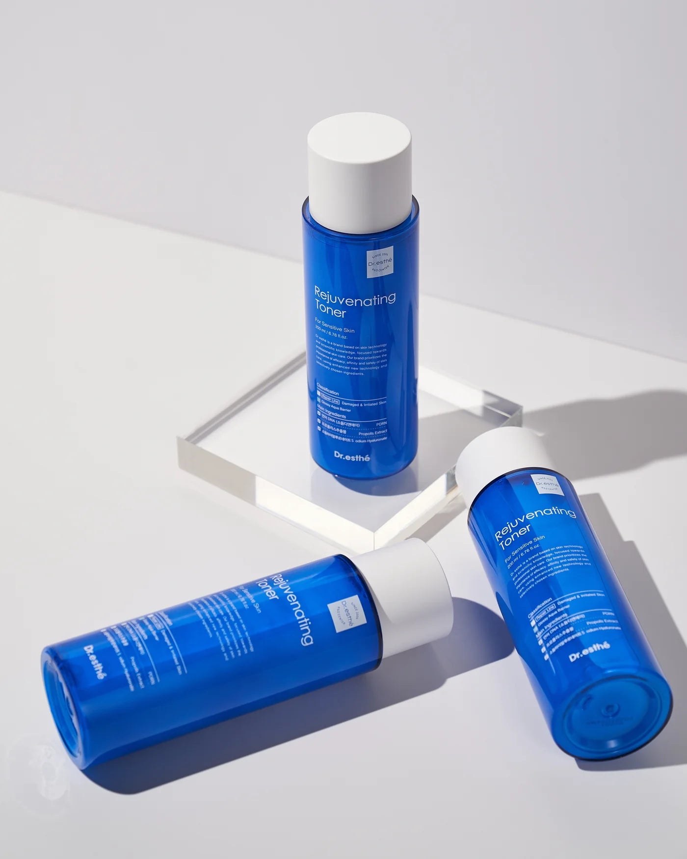 Three blue skincare bottles with white caps on a reflective surface.
