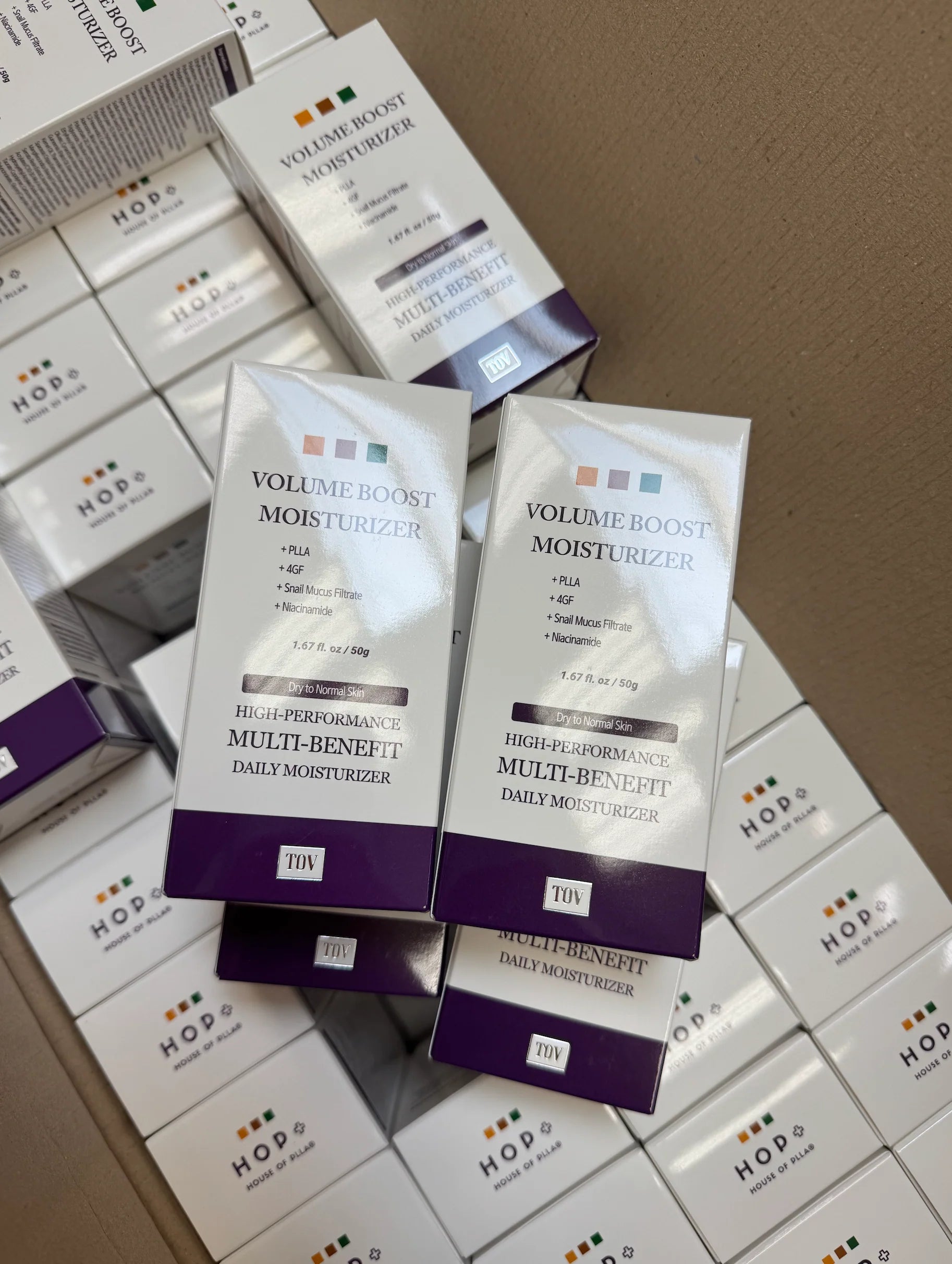 Stack of HOP+ Volume Boost Moisturizer retail boxes, showing packaging listing PLLA, 4GF, Snail Mucus Filtrate, and Niacinamide.
