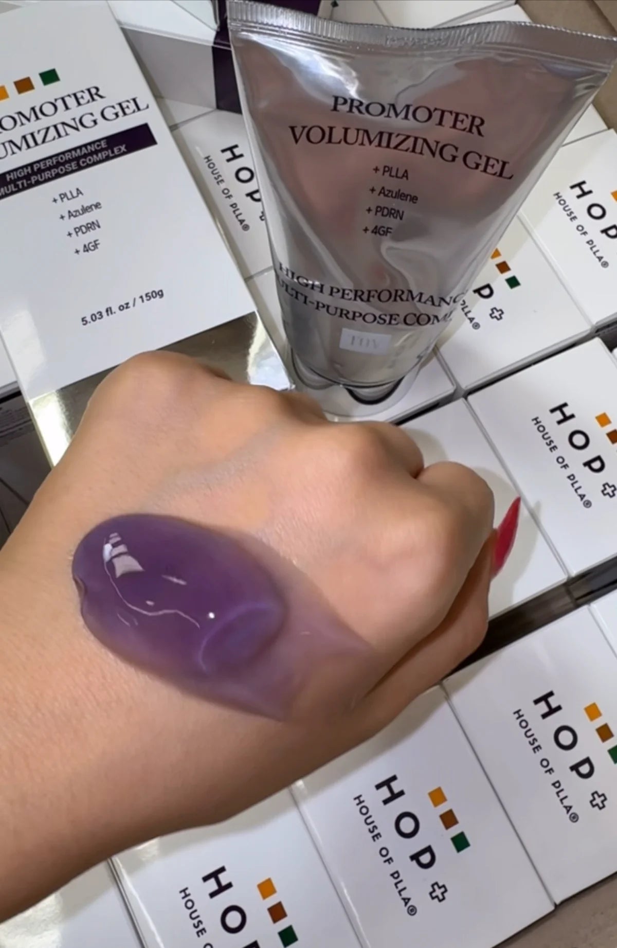 Swatch of purple Promoter Volumizing Gel applied to the back of a hand, shown next to the product tube and HOP+ House of PLLA packaging.
